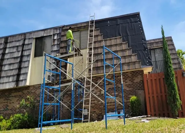 A man working on a stone-coated steel roof next to an old cedar shake mansard roof.